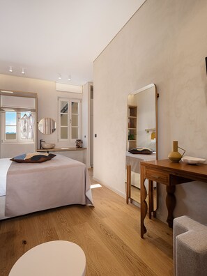 A bedroom with a bed, a wooden desk, a chair, a round table, a mirror, and a window with a view. - Casa Modiano (Chania)