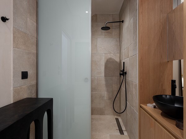 A modern bathroom with a glass shower enclosure, a wooden vanity, and a black sink.