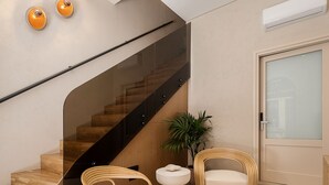 A modern interior with a wooden staircase, two wicker chairs, a small white table, and a potted plant. - Casa Modiano (Chania)