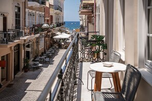 Varanda com vista para uma rua costeira, mobiliário de exterior e vasos de plantas.