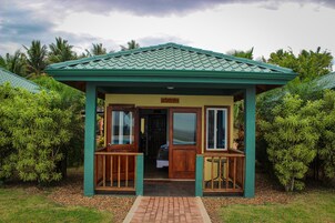 A small, single-story structure with a green roof and wooden exterior, surrounded by lush greenery.