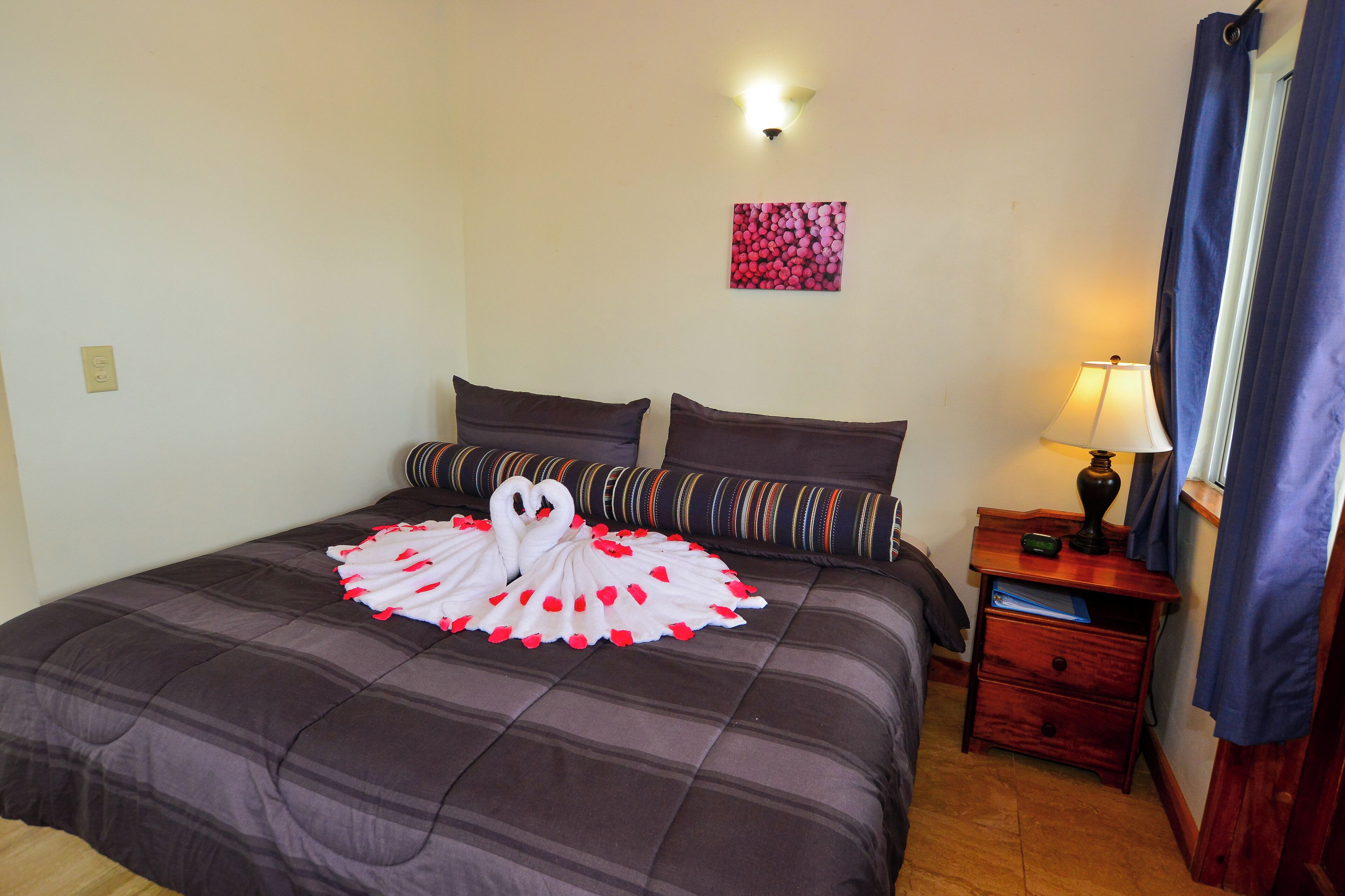 Una cama bien tendida con una toalla decorativa con forma de cisne, una lámpara de pared y una mesita de noche con lámpara.