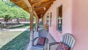 A covered porch with two chairs and a table, a pink building, and a tree in the background. - Arizona Desert Vacation Rental w/ Pool Access! (Eloy)