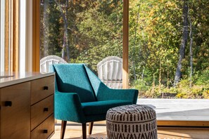 Relax in style with a view of the forest from this cozy space, featuring a comfortable armchair and a unique chair with a geometric backrest.
