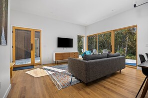 Relax in this stylish living room with a large flat-screen TV, comfortable sofa, and sliding glass door leading to an outdoor area with a view.