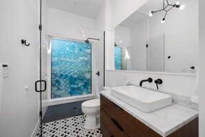 Un baño moderno con cabina de ducha de vidrio, un lavamanos blanco y un espejo grande.