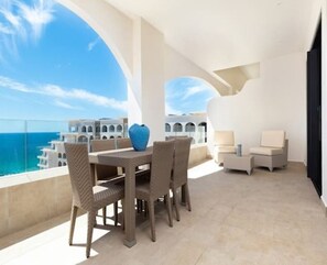 Enjoy ocean views from this expansive balcony with a wicker dining table and comfortable seating.