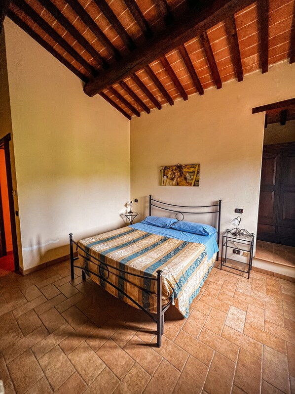 Un dormitorio con cama, mesita de noche, un cuadro y piso de baldosas.
