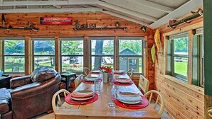 A wooden cabin with a dining area set for a meal, large windows, and a view of the outdoors. - Cozy Lakefront Cabin w/ Sandy Beach & Bunkhouse! (Deerwood)