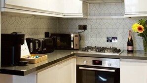 A modern kitchen with white cabinets, a Bosch oven, a microwave, a coffee machine, and a gas stove. - Avari - Luxury 2BR Apartment • Steps from Victoria (London)