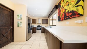 A modern kitchen with a long counter, wooden cabinets, and a large abstract painting on the wall. - Freshly Updated 3BR With Pool Walk to the Beach Casa Luz de Luna (Tempate)