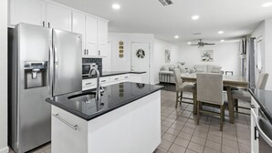 A modern kitchen with white cabinets, a stainless steel refrigerator, a built-in water dispenser, and a black countertop.