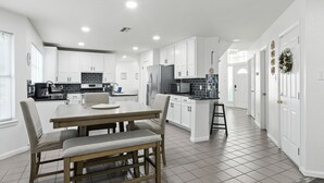 A modern kitchen with white cabinets, a central island, and a dining area with a wooden table and chairs.