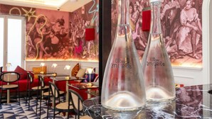 Deux bouteilles de verre vides, portant l’étiquette « UPON angels », sont posées sur une table en marbre dans un restaurant aux sièges rouges, avec une fresque murale en arrière-plan.