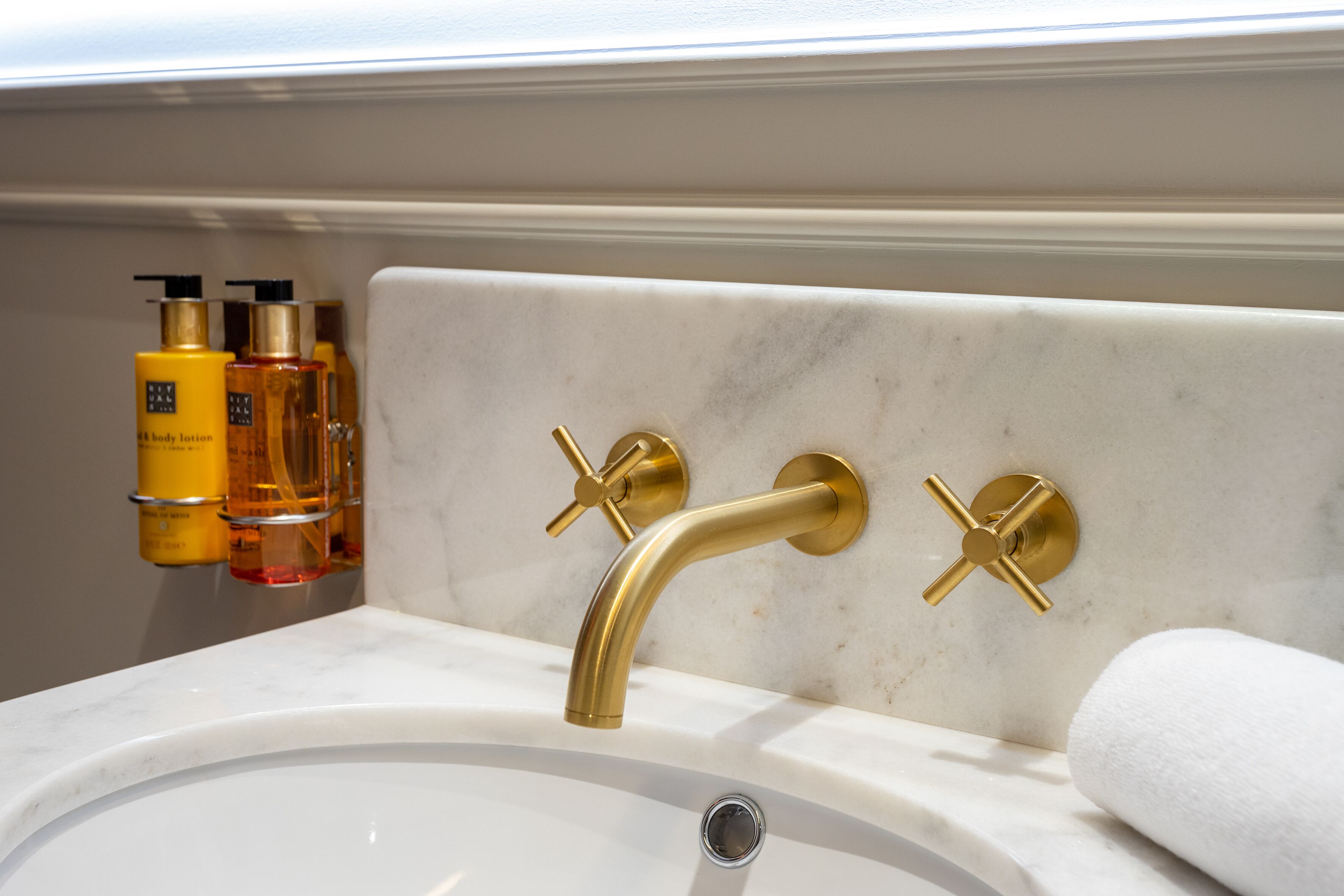 Un bagno con lavabo in marmo bianco, rubinetti dorati e articoli da toilette a parete.