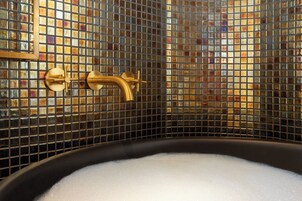 Una vasca da bagno con un rubinetto dorato e una parete rivestita di mosaici.