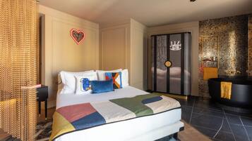 Une chambre d’hôtel moderne avec un grand lit, une baignoire noire et un mur décoratif agrémenté d’un luminaire en forme de cœur.