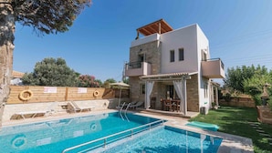 A two-story house with a swimming pool, a covered patio, and a garden.