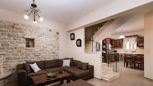 A living room with a stone wall, a brown sectional sofa, a wooden coffee table, and a staircase leading to a kitchen.