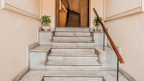 A marble staircase with a handrail, leading to a landing with a view of a staircase in the background.