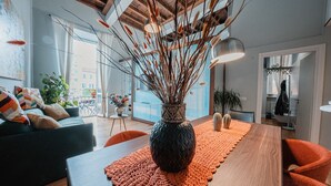 A modern living room with a wooden dining table, orange rug, and a decorative vase.