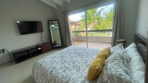 Ein Schlafzimmer mit Bett, Fernseher, Spiegel und einem Balkon mit Blick auf Grünflächen.