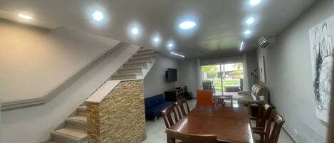 A spacious living area with a dining table, chairs, a blue sofa, and a stone accent wall. A staircase with a stone base leads to an upper level.