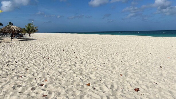 Ein weiter Sandstrand mit blauem Himmel und vereinzelten Wolken.