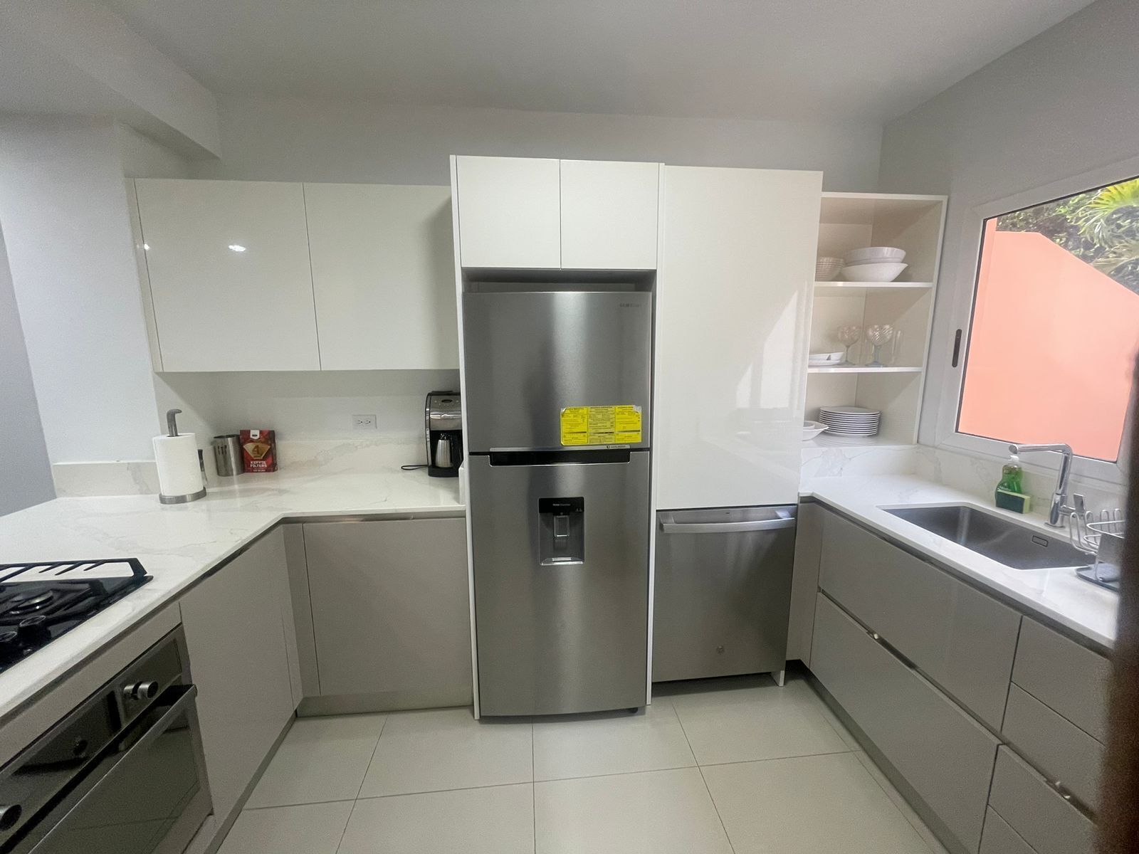 A compact kitchen with white cabinets, a stainless steel refrigerator, a built-in dishwasher, and a gas stove.