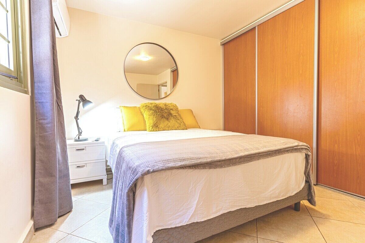 A bedroom with a bed, a nightstand, a lamp, a mirror, and a wardrobe.