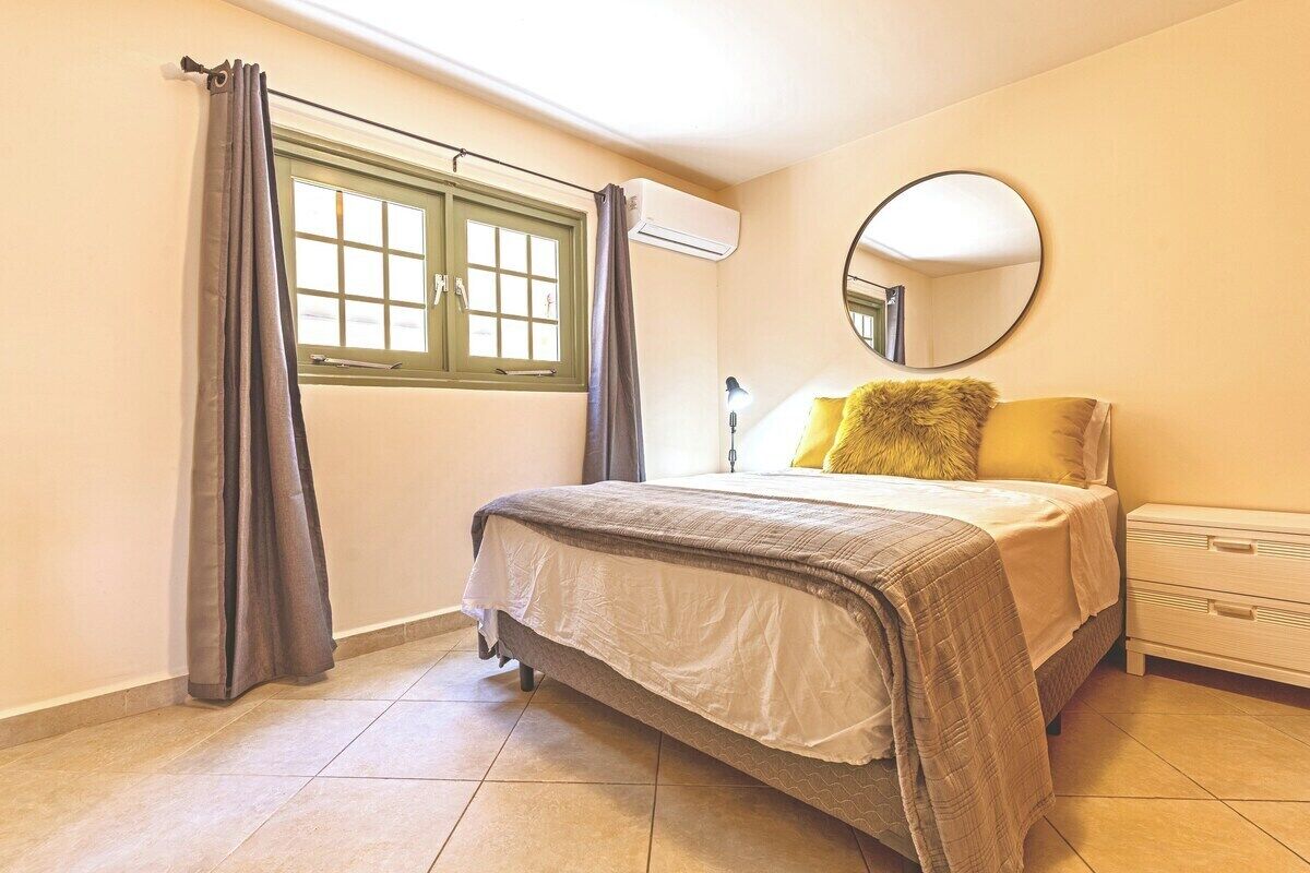 A bedroom with a bed, a bedside table, a mirror, and a window with curtains.