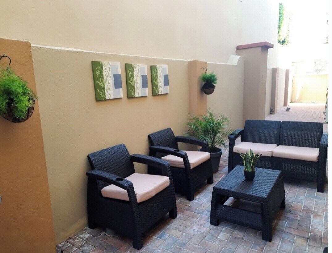 Ein Außenbereich mit einer Terrasse, Korbmöbeln, darunter Stühle und eine Couch, sowie Pflanzgefäßen.