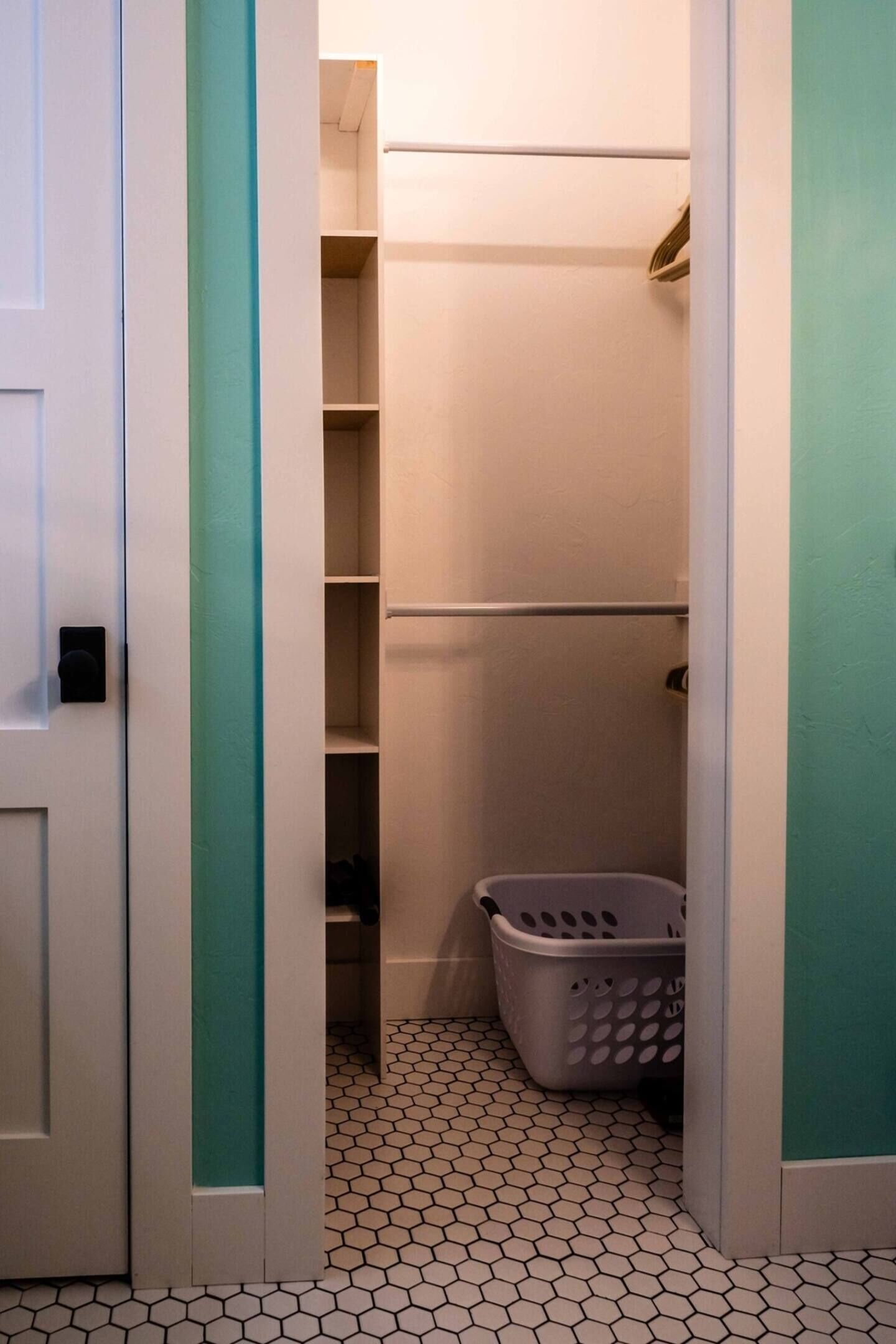 A narrow hallway with a closet, a laundry basket, and a tiled floor.