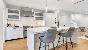 A modern kitchen with white cabinetry, a central island with bar stools, and a stainless steel range hood. - 1408 N Poinsettia Pl (Los Angeles)