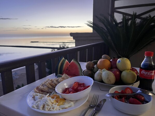 A table with breakfast items including fruits, bread, and a Coca-Cola bottle, overlooking a scenic view.