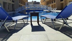 Un espace piscine avec des chaises longues bleues et une petite table, entouré d’immeubles à plusieurs étages.