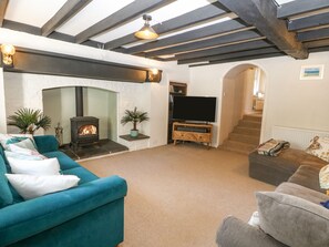 A living room with a fireplace, a television, and a staircase leading upstairs. - Mill House (Pwllheli)
