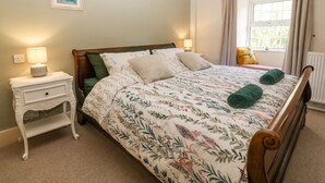 Uma cama bem arrumada com roupa de cama florida, uma mesa de cabeceira com abajur e uma janela com cortinas.