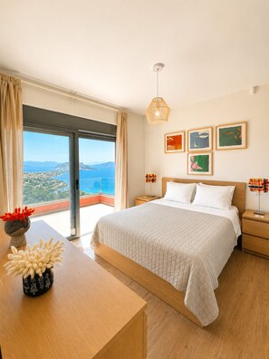 Une chambre à coucher avec un grand lit, une table de chevet, une lampe de chevet, un luminaire suspendu et une vue sur la mer.