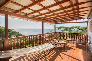 A wooden deck with a hammock, a table, and chairs, overlooking a lush landscape and the sea. - Experience Local Culture: Nutmeg Superior Room at Mount Edgecombe Boutique Hotel (Victoria)