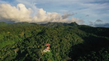 Un paysage montagneux avec une maison dotée d’un toit rouge, nichée au milieu d’une végétation luxuriante.
