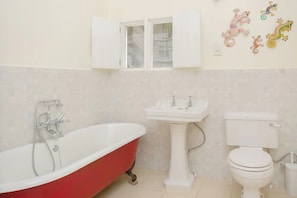 A bathroom with a red clawfoot bathtub, a white pedestal sink, and a white toilet.