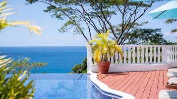 An infinity pool with a view of the ocean, a white fence, and a potted plant.