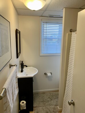 A small bathroom with a white sink, a toilet, and a window with blinds.