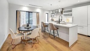 Una cocina moderna con una isla central, armarios blancos y una zona de comedor con una mesa redonda y sillas.