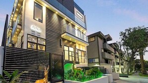 Un edificio moderno de varios pisos con fachada de vidrio, número visible y un jardín delantero con césped y una escultura de venado.