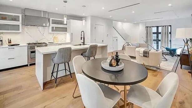 Una cocina moderna con una isla central, una zona de comedor con una mesa redonda y sillas, y un espacio de sala de estar con un sofá y una mesa de centro.