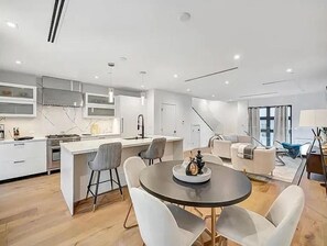 Een moderne keuken met een centraal eiland, een eethoek met een ronde tafel en stoelen, en een zithoek met een bank en salontafel.