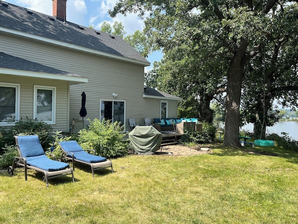 Une maison dotée d’un patio couvert, de deux chaises longues, d’une table abritée et offrant une vue sur un lac.