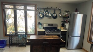 Una cocina moderna con estufa a gas, refrigerador de acero inoxidable y ollas colgantes.